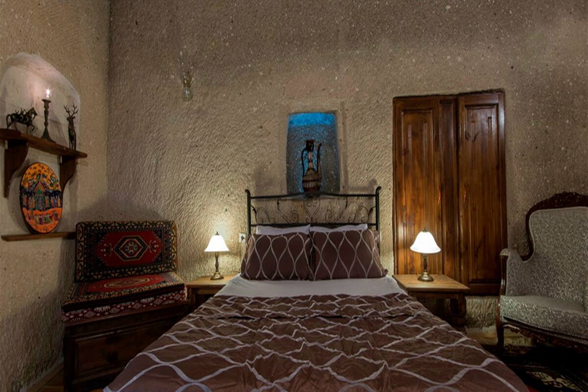 Un dormitorio con cama, un armario de madera, una silla, una mesita de noche, una lámpara y una pared con un cuadro y una estantería con adornos.
