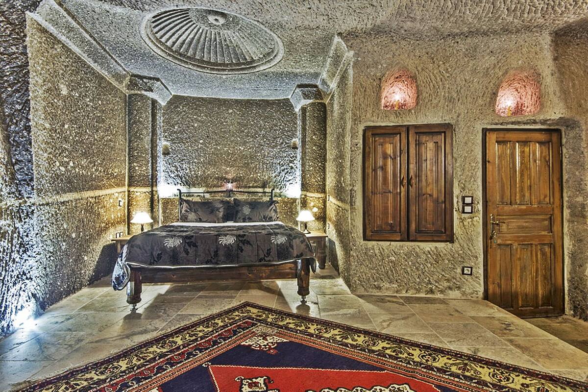 Un dormitorio con una cama, dos puertas de madera, un tapiz estampado y paredes de piedra.