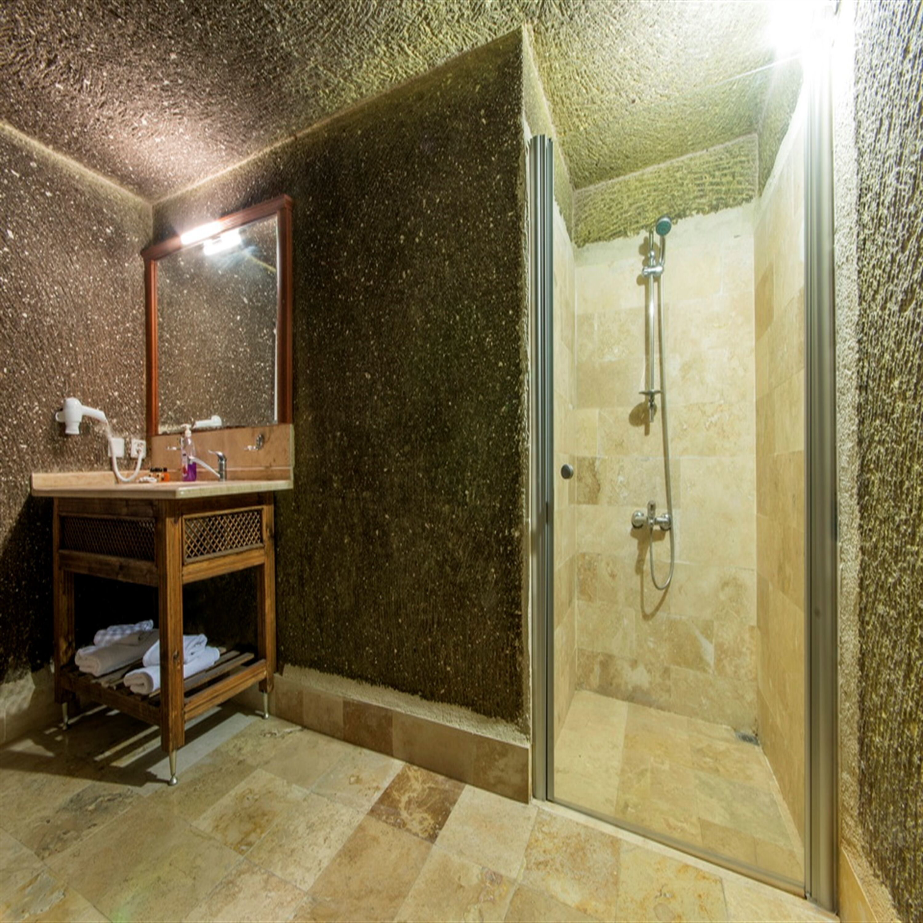 A bathroom with a glass-enclosed shower, a wooden vanity with a mirror, and a shelf with towels.