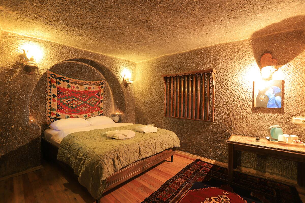 Una habitación con una cama, un banco de madera, una lámpara de pared y una pared con textura.