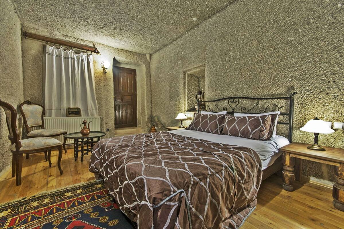 Un dormitorio con una cama grande, una silla de madera, una mesita y una lámpara.