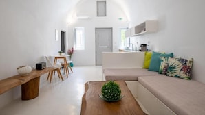 A modern living room with a sofa, a wooden coffee table, a dining area with chairs, and a kitchen area with a counter and cabinets. - Fertimo Suites (Santorini)