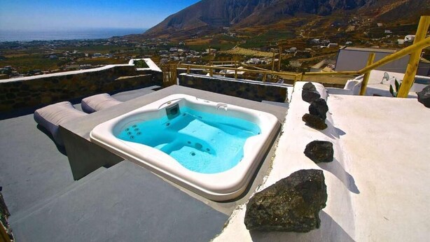 A hot tub with a mountainous backdrop, a stone wall, and a wooden deck. - Fertimo Suites (Santorini)