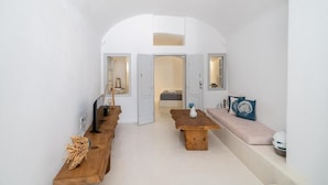 A minimalist room with a wooden bench, a small table, and a bench with cushions. - Fertimo Suites (Santorini)