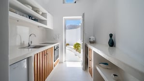 A narrow kitchen with white cabinetry, a built-in oven, and a window overlooking a mountainous landscape. - Fertimo Suites (Santorini)