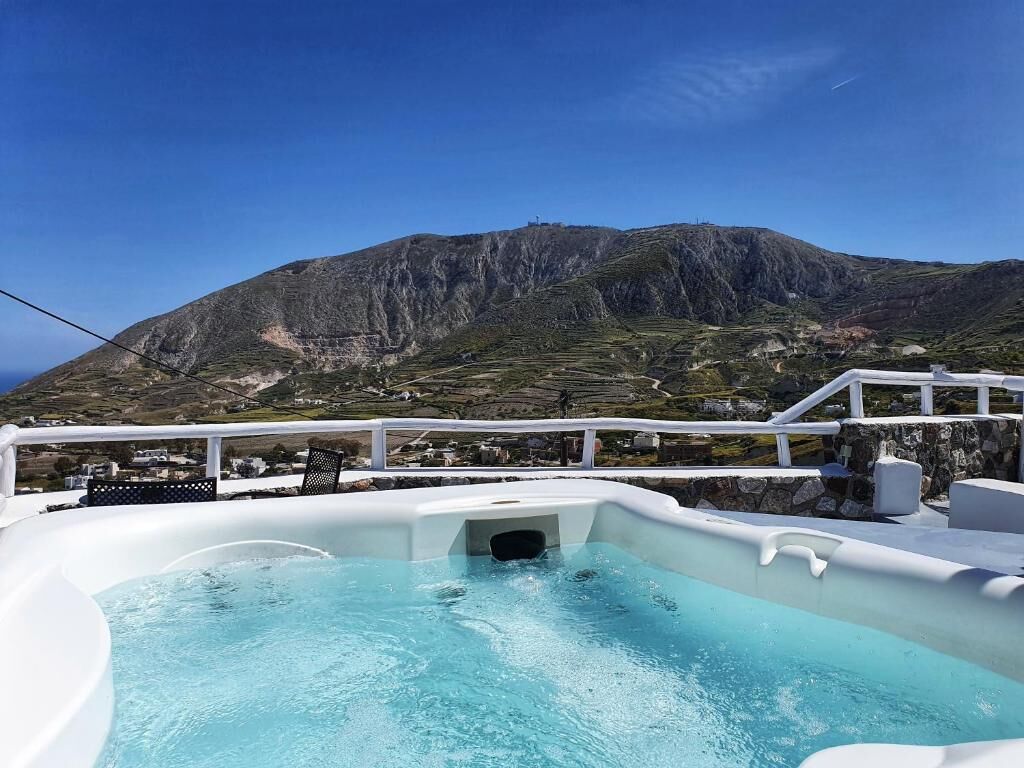 A hot tub with a mountain view, white railings, and a clear sky.