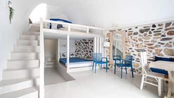 A room with a bunk bed, a dining table with chairs, and a stone wall.