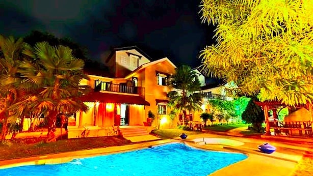 A nighttime view of a resort with a swimming pool, palm trees, and a well-lit building. - Amour Resort (Vagator)