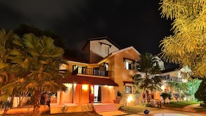 A two-story building with a balcony, surrounded by palm trees and a well-lit garden area. - Amour Resort (Vagator)