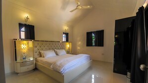 A bedroom with a large bed, two bedside tables, a ceiling fan, and a window with curtains. - Amour Resort (Vagator)