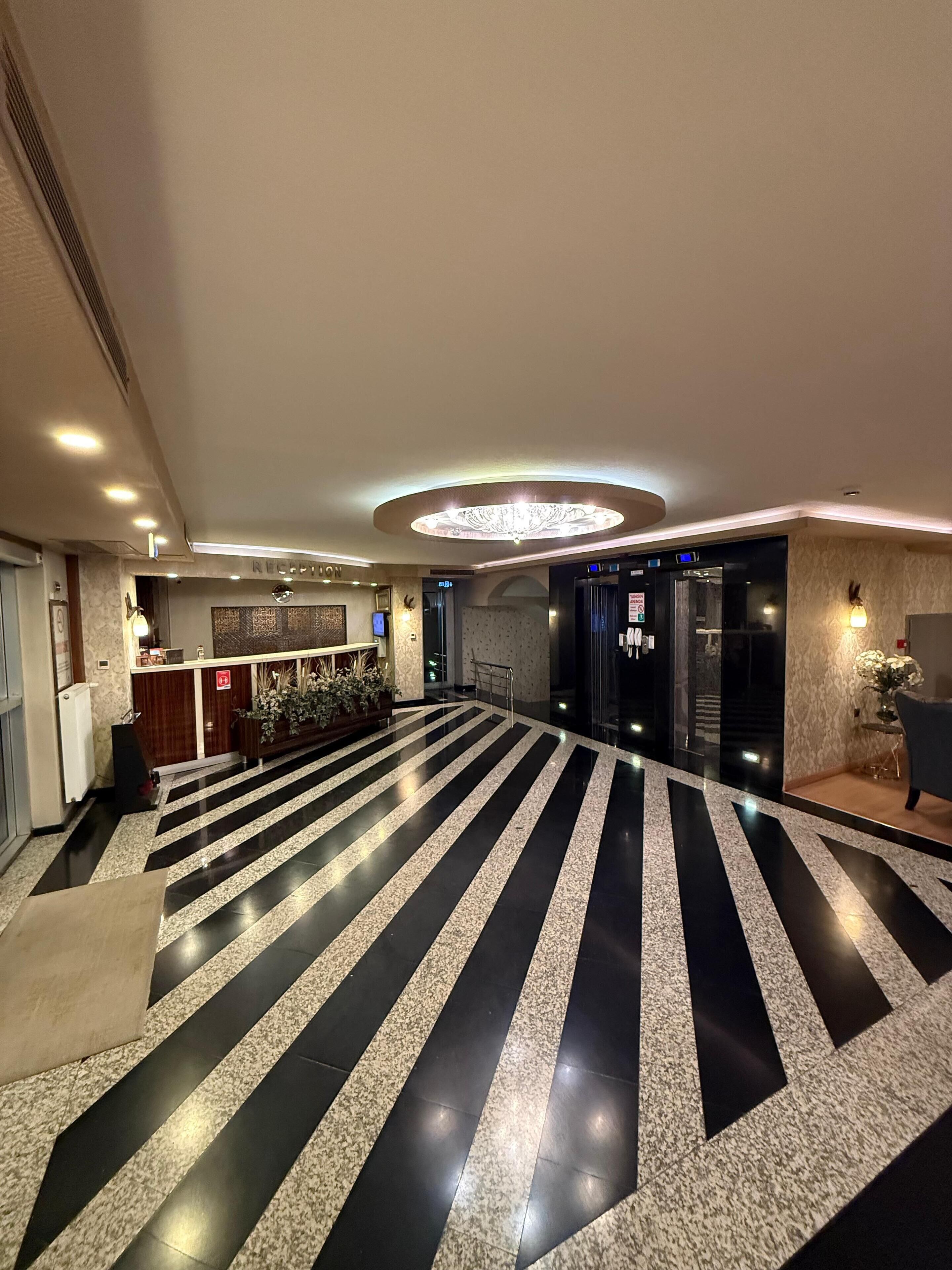 A hotel lobby with a black and white striped floor, a reception desk, and a modern chandelier.