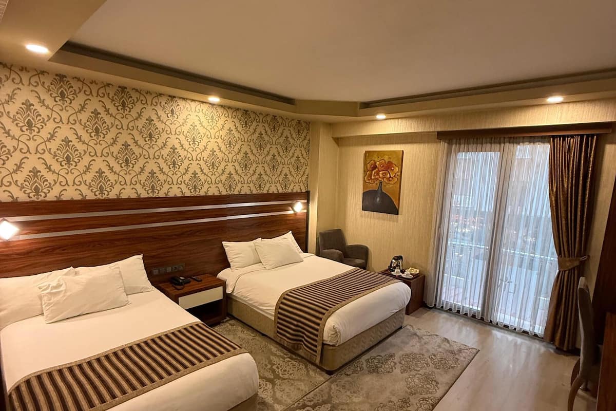 A hotel room with two beds, a large window with curtains, a painting on the wall, and a wooden headboard.