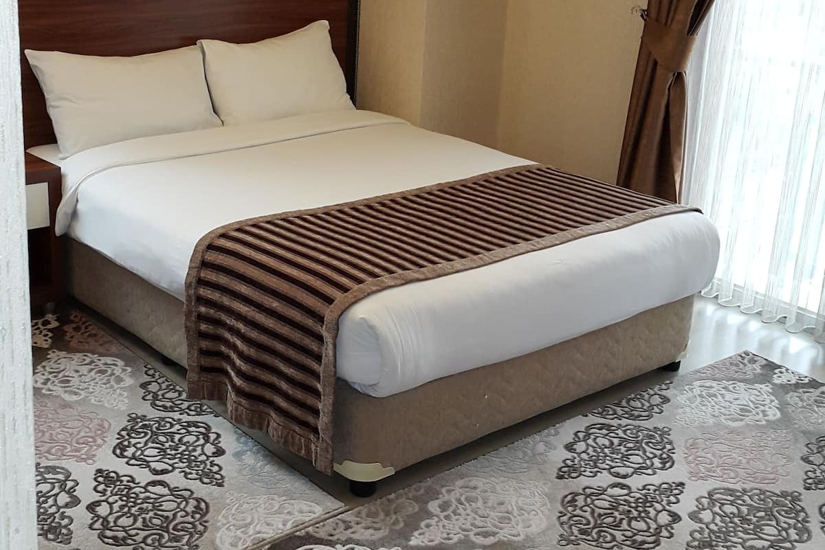 A neatly made bed with a headboard, a patterned rug, and a wall with a decorative piece.