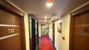 Un couloir d’hôtel avec un tapis rouge, des portes en bois et un panneau au plafond indiquant la sortie.