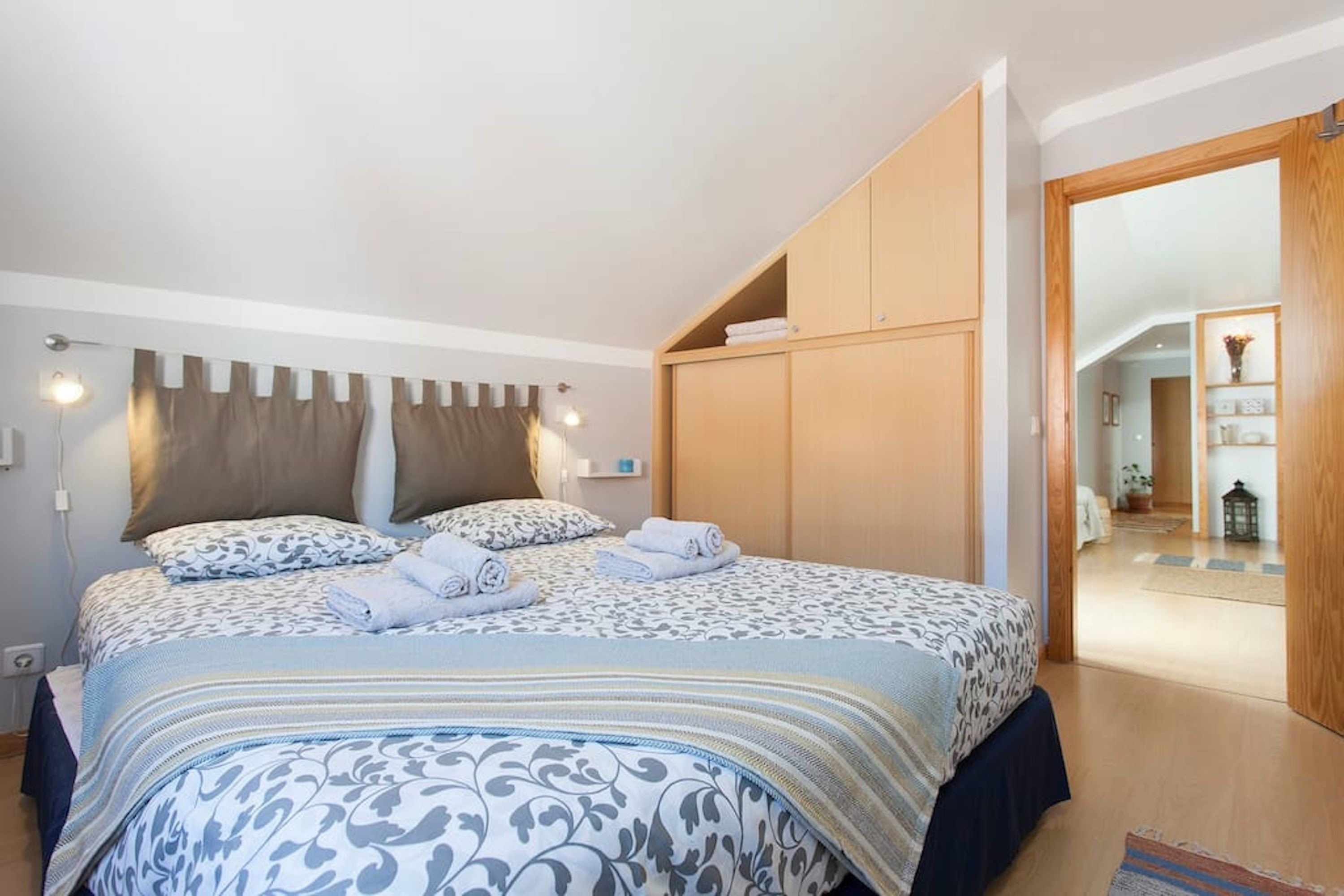 A bedroom with a bed, a wardrobe, and a hallway leading to another room.