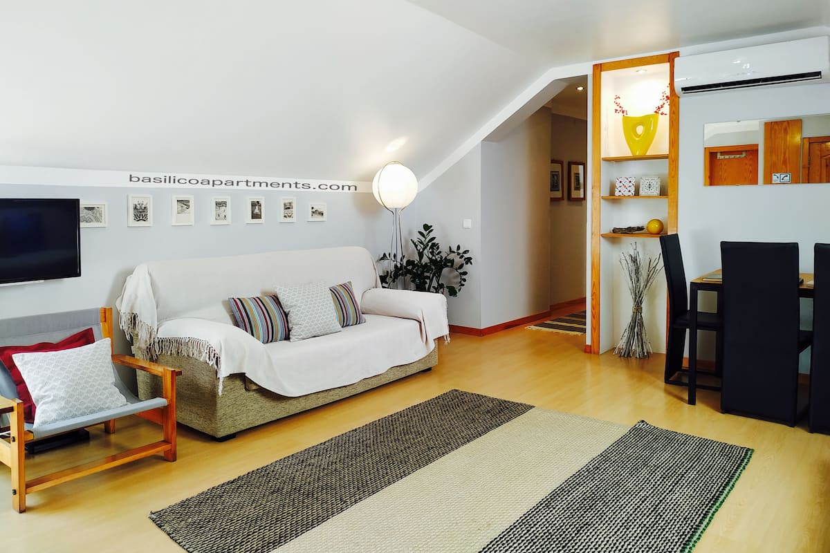 A modern living room with a sofa, a TV, and a dining area with chairs and a table.