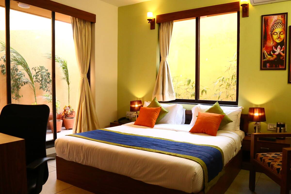 A hotel room with a bed, a chair, a desk, and a window with curtains.