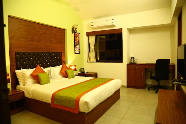 A hotel room with a large bed, a desk, a chair, and an air conditioning unit.