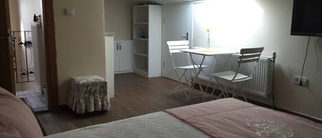 A bedroom with a bed, a small table, two chairs, a radiator, and a TV on the wall.