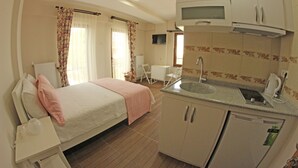 A compact hotel room with a bed, a small kitchenette, a bathroom, and a TV mounted on the wall. - Ede Apart Hotel (Ezine)