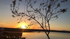 A sunset over a calm lake with a picnic table and a tree in the foreground. - Ede Apart Hotel (Ezine)