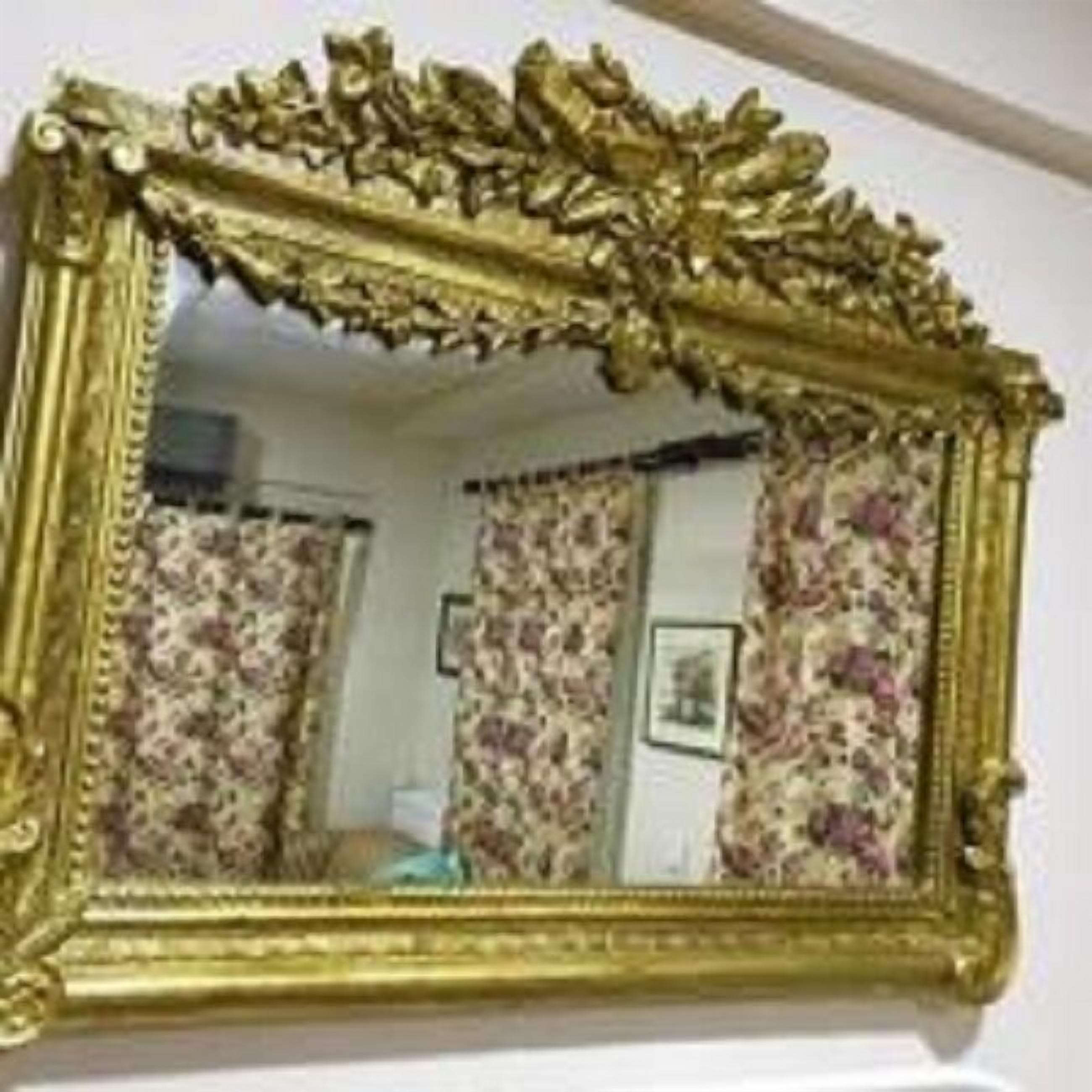 A room with a large ornate mirror, floral curtains, and a framed picture on the wall.