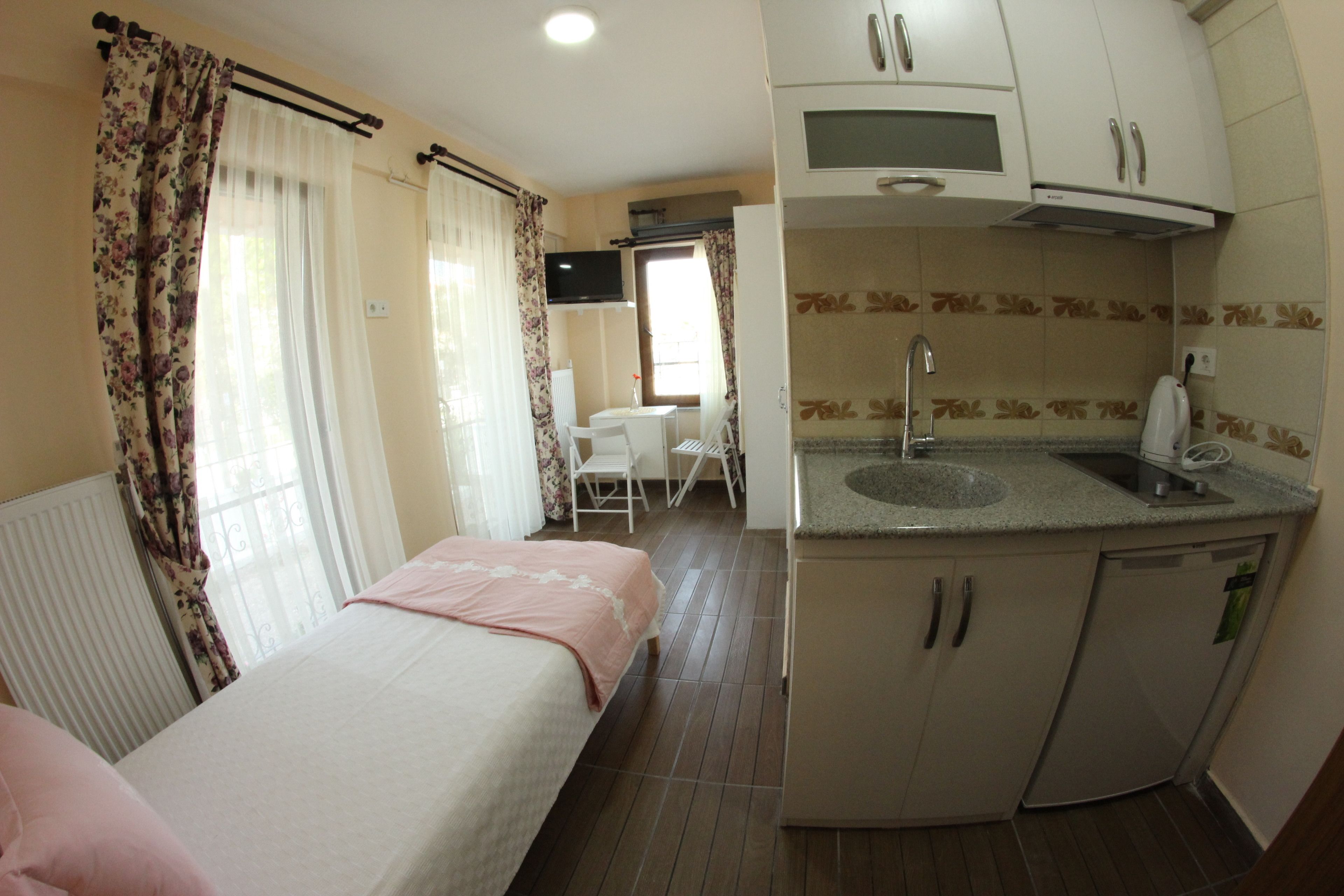 A compact hotel room with a bed, a small kitchenette, a dining area, and a television.