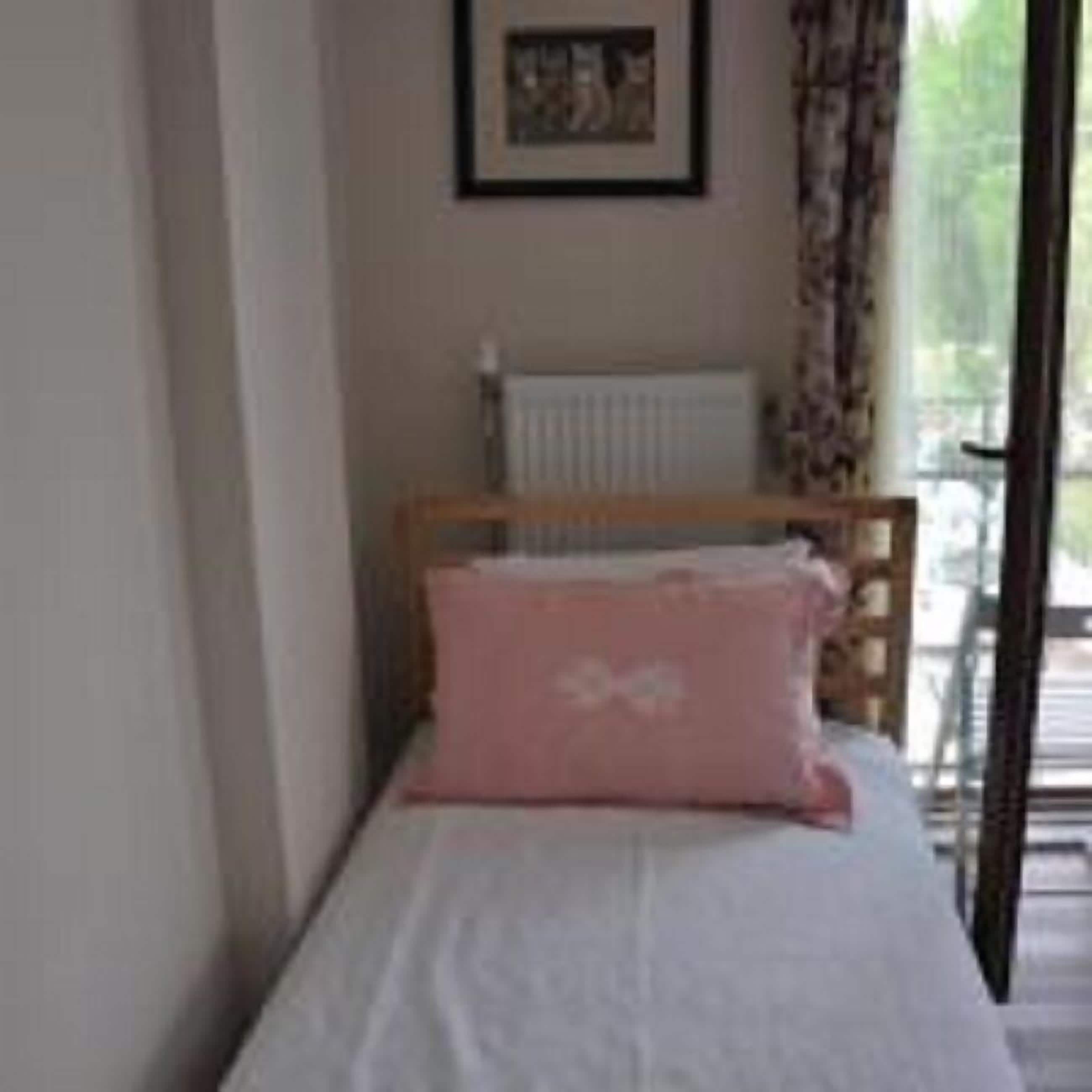 A bedroom with a single bed, a radiator, and a window with curtains.