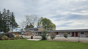Un espacio cubierto de césped con un edificio que parece un motel o un pequeño hotel. Se ven árboles y un cielo despejado al fondo.