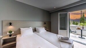 Habitación de hotel moderna con una cama grande, una mesita de noche con lámpara, una planta pequeña y vistas al exterior.