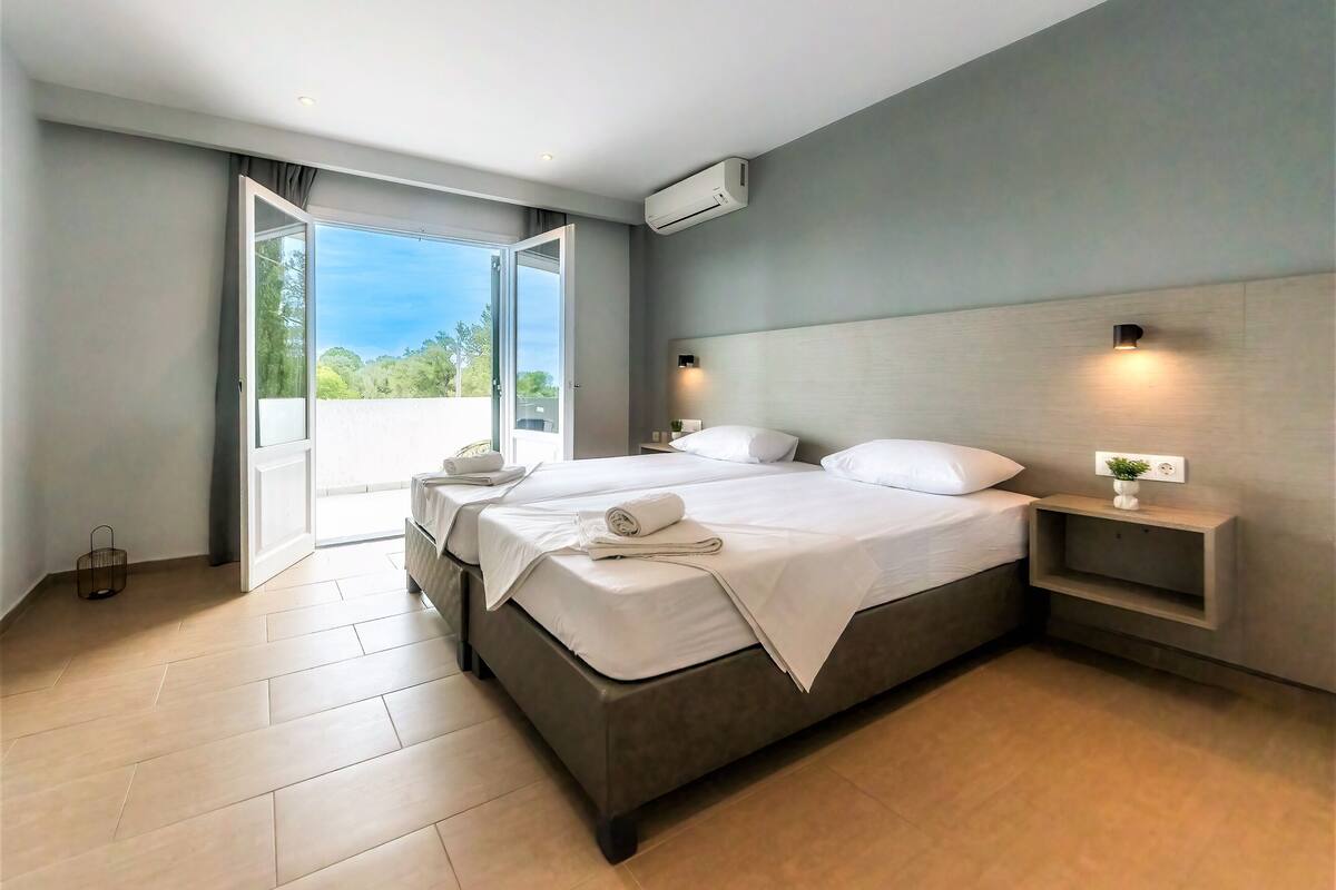 A modern hotel room with a large bed, a bedside table, a nightstand, and an air conditioning unit.