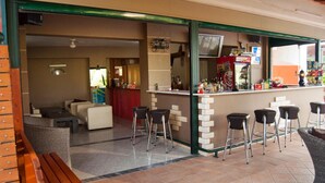 Un área de bar al aire libre con taburetes, una barra con varias botellas y un espacio de estar con un sofá y sillones.