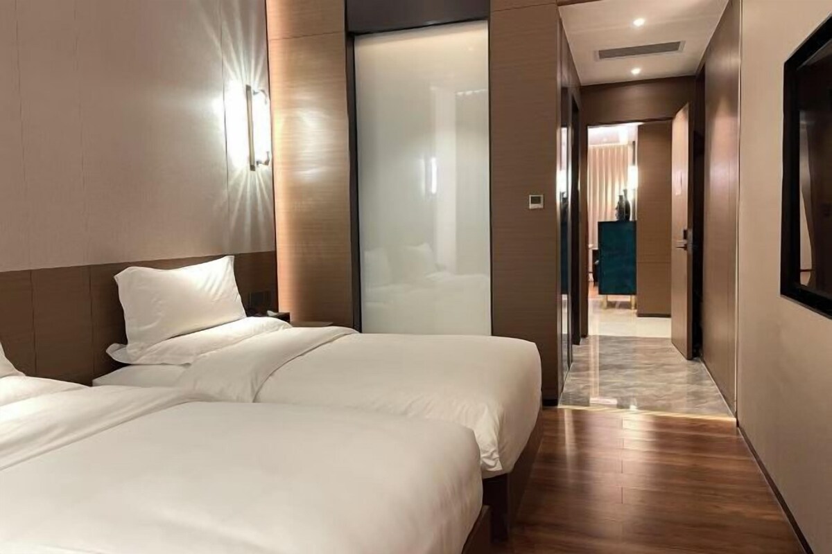 A hotel room with two beds, a wooden floor, and a hallway leading to another room.