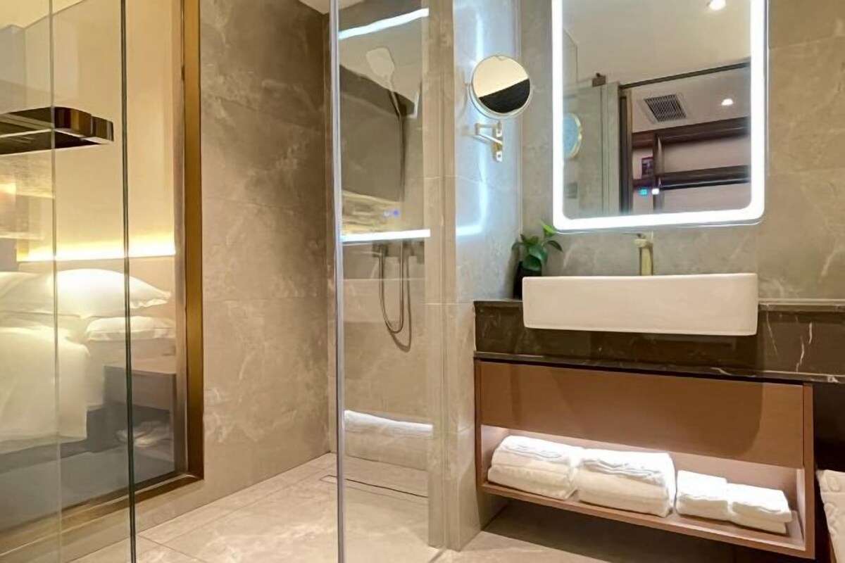 A modern bathroom with a glass-enclosed shower, a marble sink, and a built-in shelf with towels.