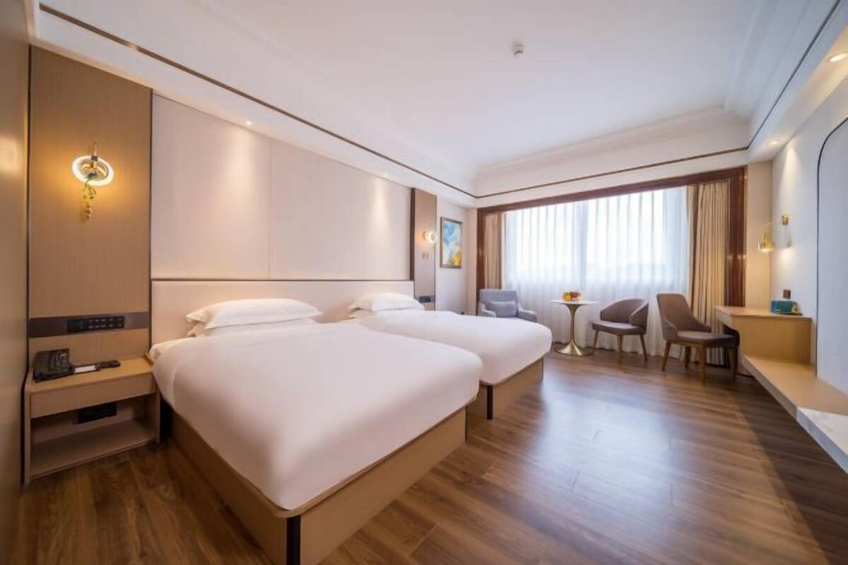 A hotel room with two beds, a desk, a chair, and a small table.