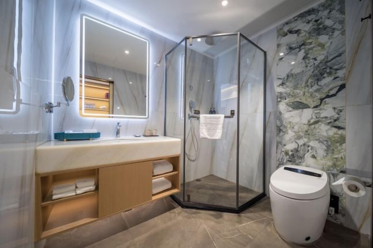 A modern bathroom with a glass-enclosed shower, a vanity with a mirror, and marble walls.