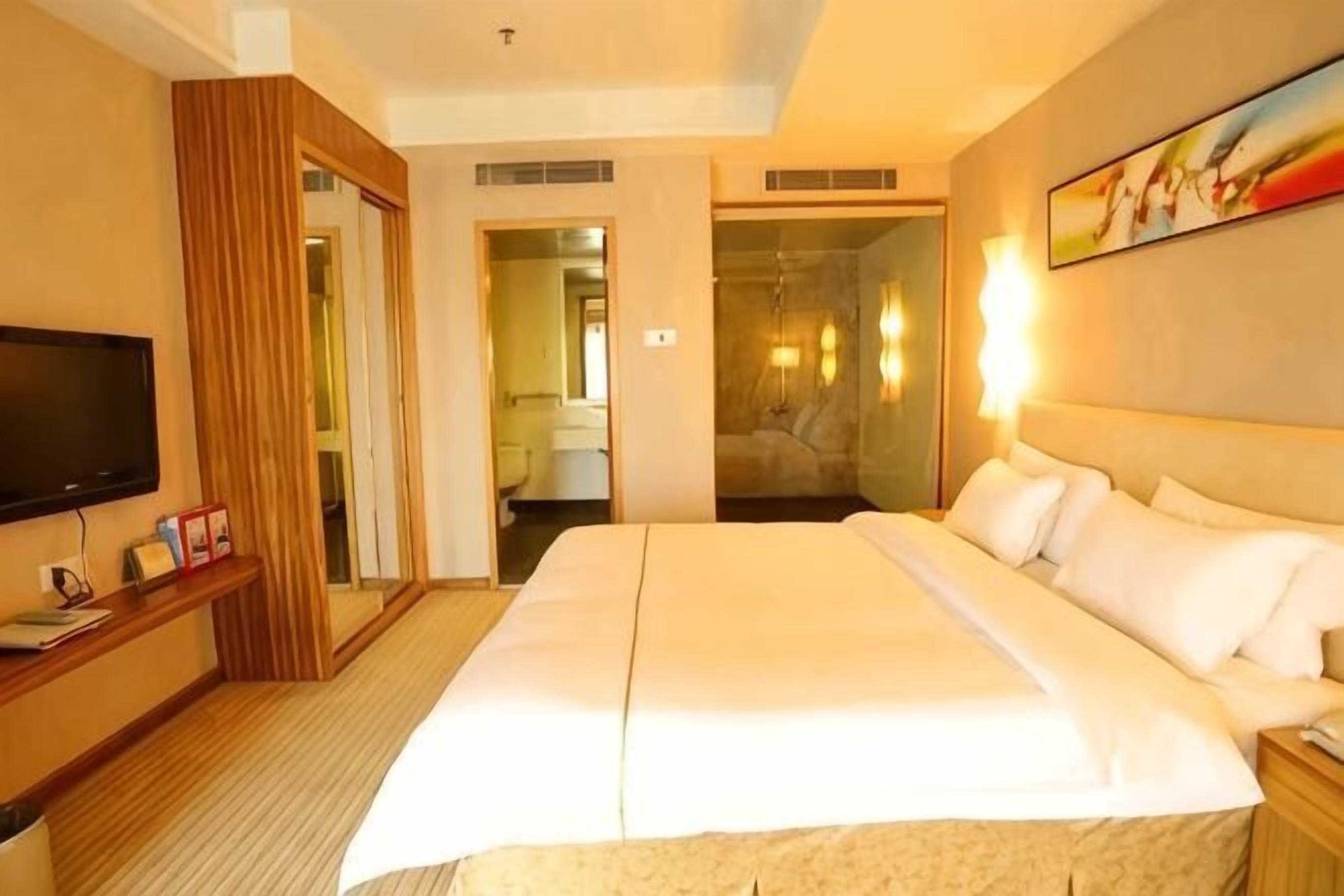 A hotel room with a large bed, a television, a bedside table, and a painting on the wall.