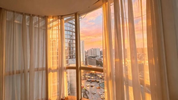 A room with a curved window, curtains, and a view of a cityscape. - Dreamland Hotel Huizhou (Huizhou)