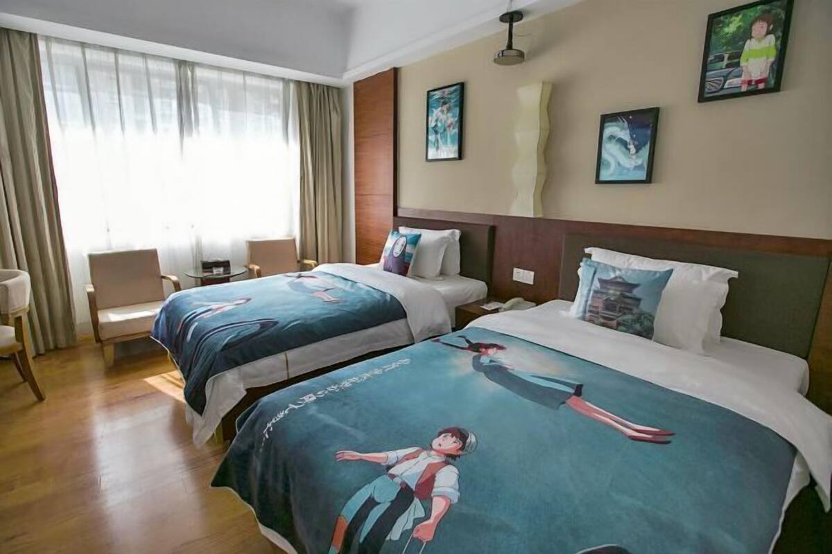 Hotellihuone, jossa on kaksi sänkyä, oleskelualue tuoleineen sekä taideteoksia seinillä.