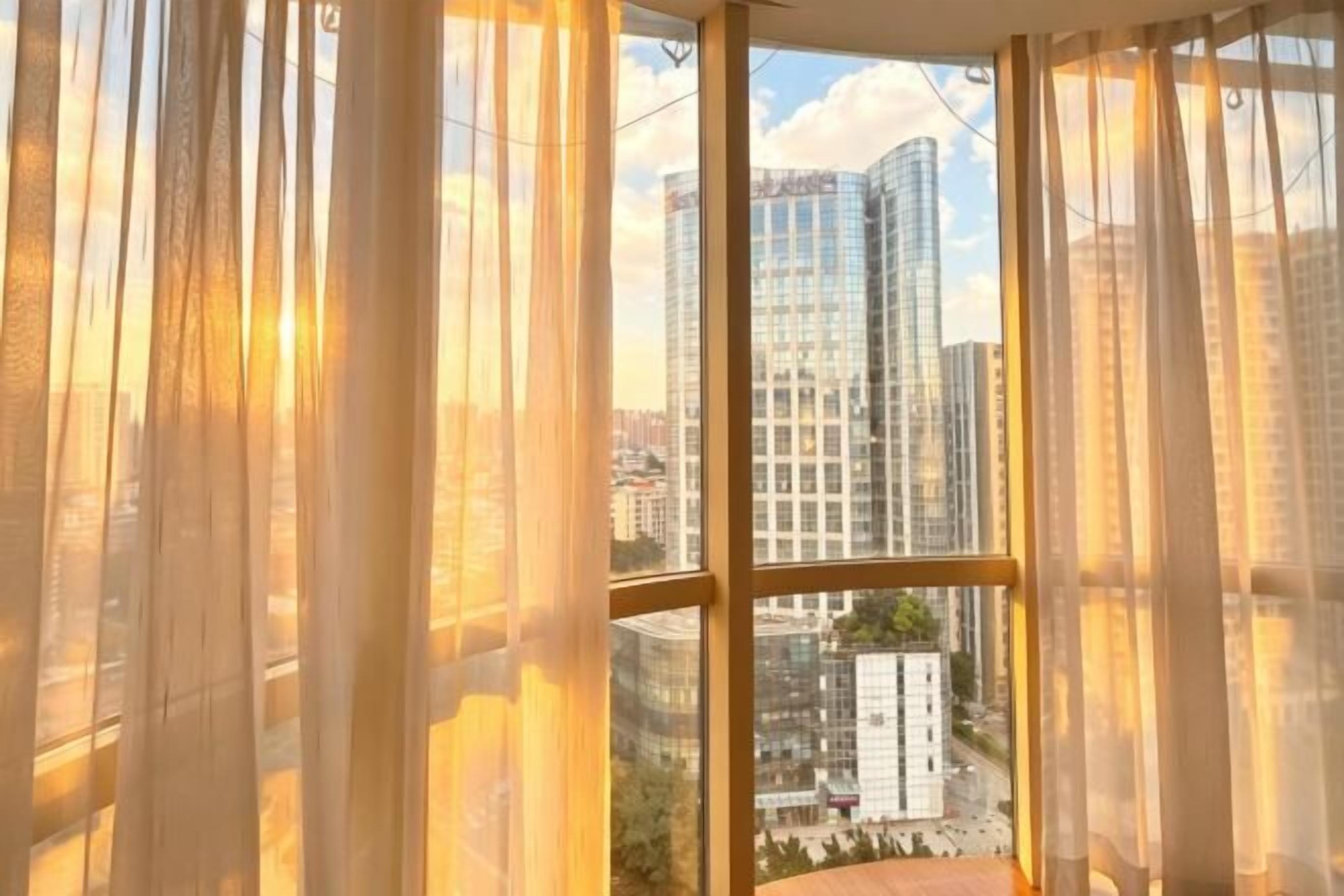 Una habitación con un ventanal, cortinas y vistas de edificios altos.