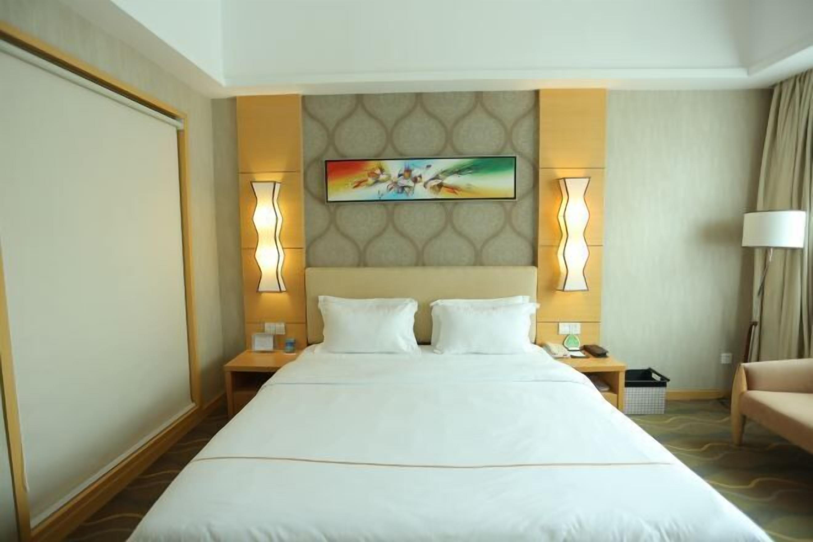 Une chambre d’hôtel avec un grand lit, deux tables de chevet, une petite table, une lampe et un tableau au mur.