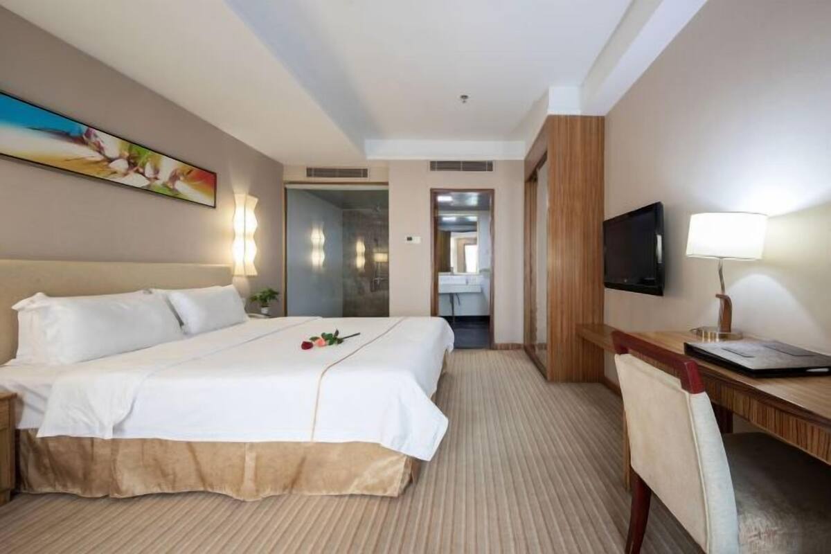 Hotellihuone, jossa on suuri sänky, työpöytä, televisio ja taulu seinällä.