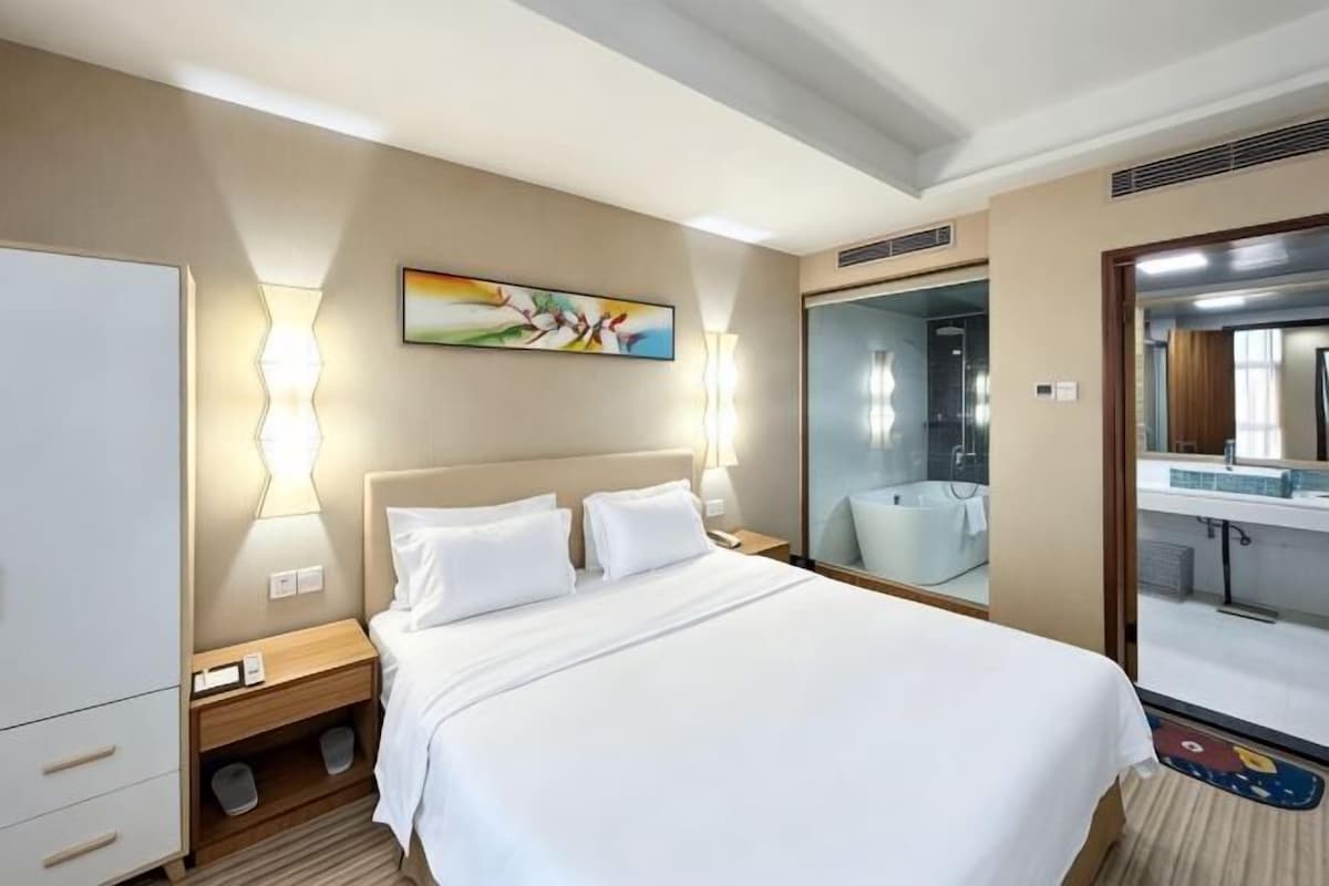 Una habitación de hotel con cama, mesitas de noche, un espejo, un cuadro y un armario.