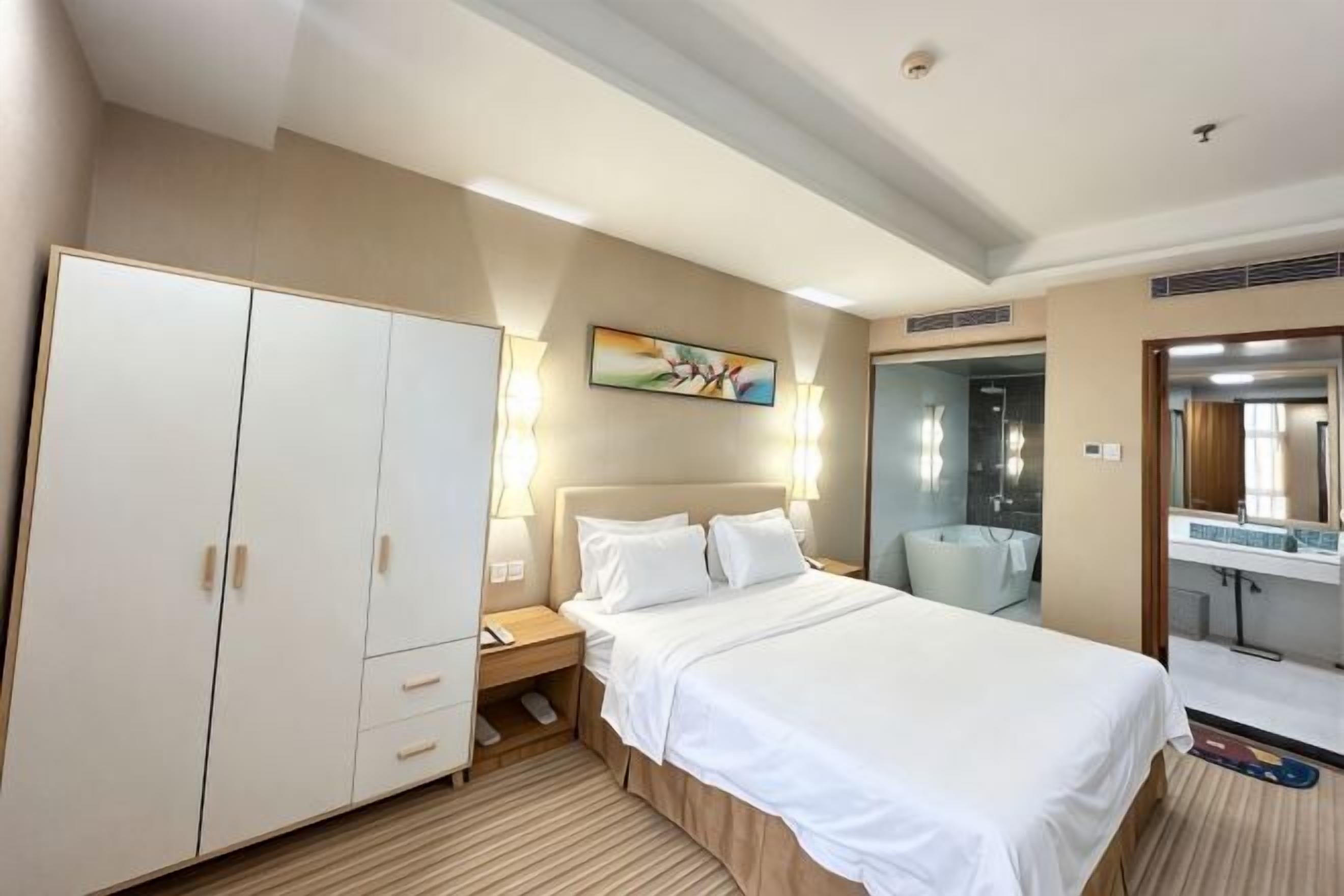A hotel room with a bed, wardrobe, bedside table, lamp, and a painting on the wall.