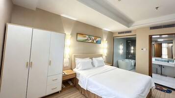A hotel room with a bed, wardrobe, bedside table, lamp, and a painting on the wall.
