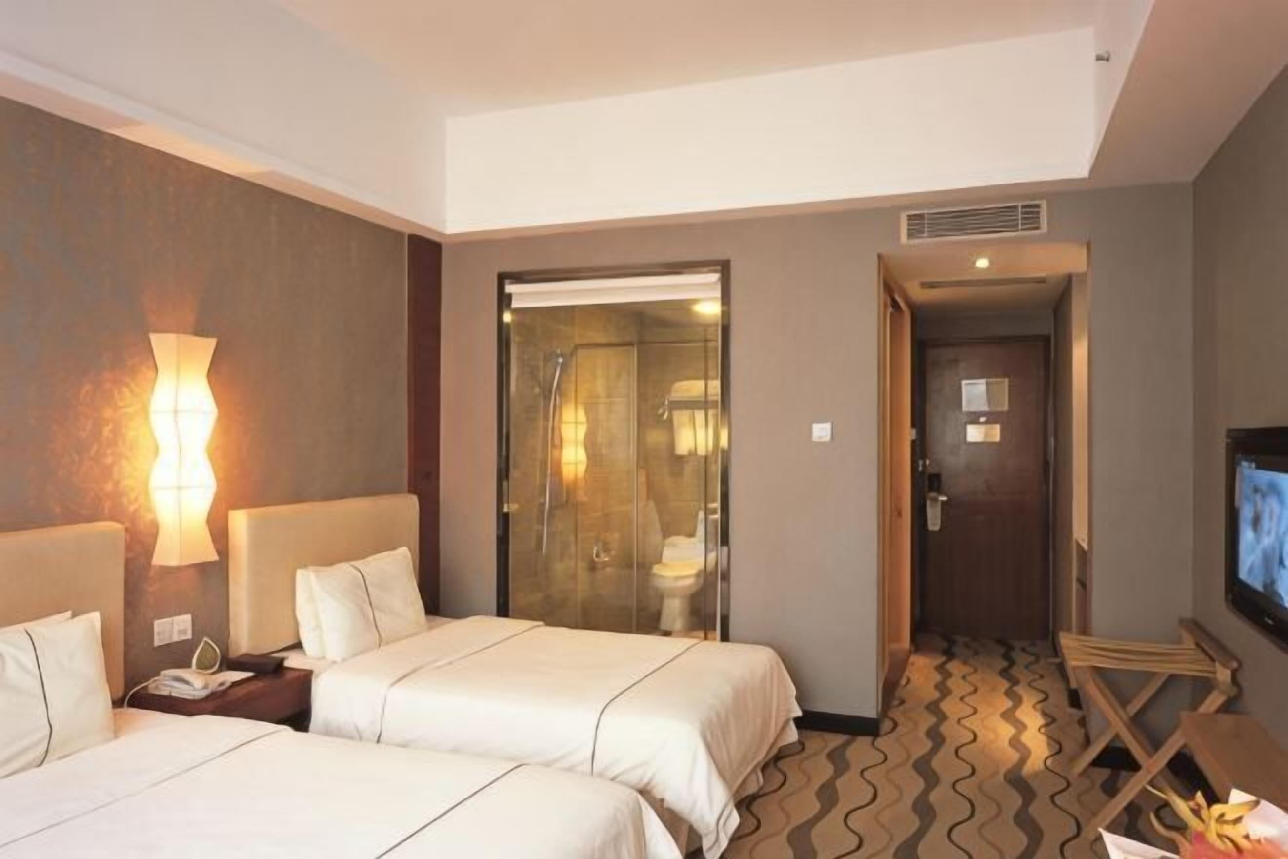 Une chambre d’hôtel avec deux lits, un espace douche, une télévision et un bureau avec une lampe.