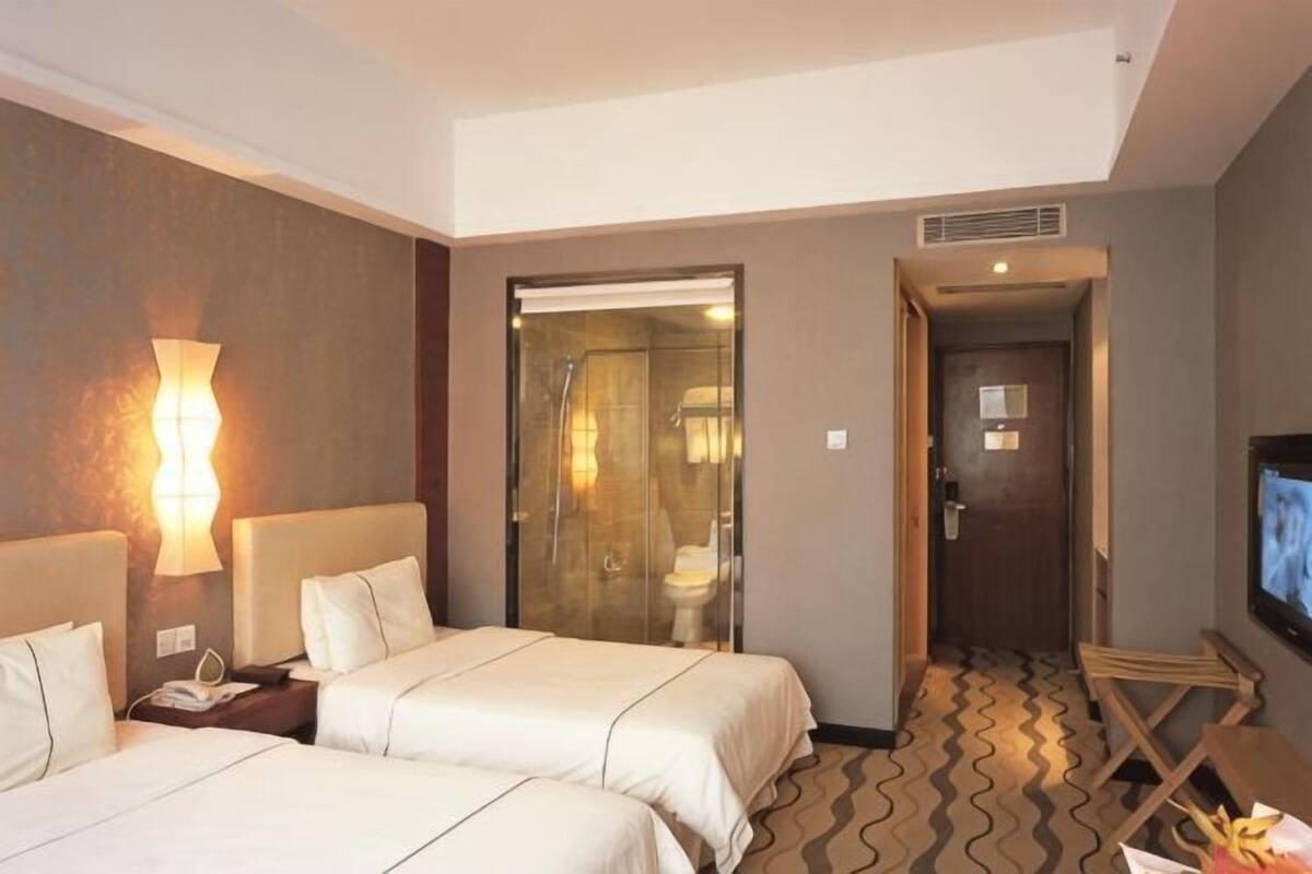 Une chambre dâhĂŽtel avec deux lits, un espace douche, une tĂ©lĂ©vision et un bureau avec une lampe.