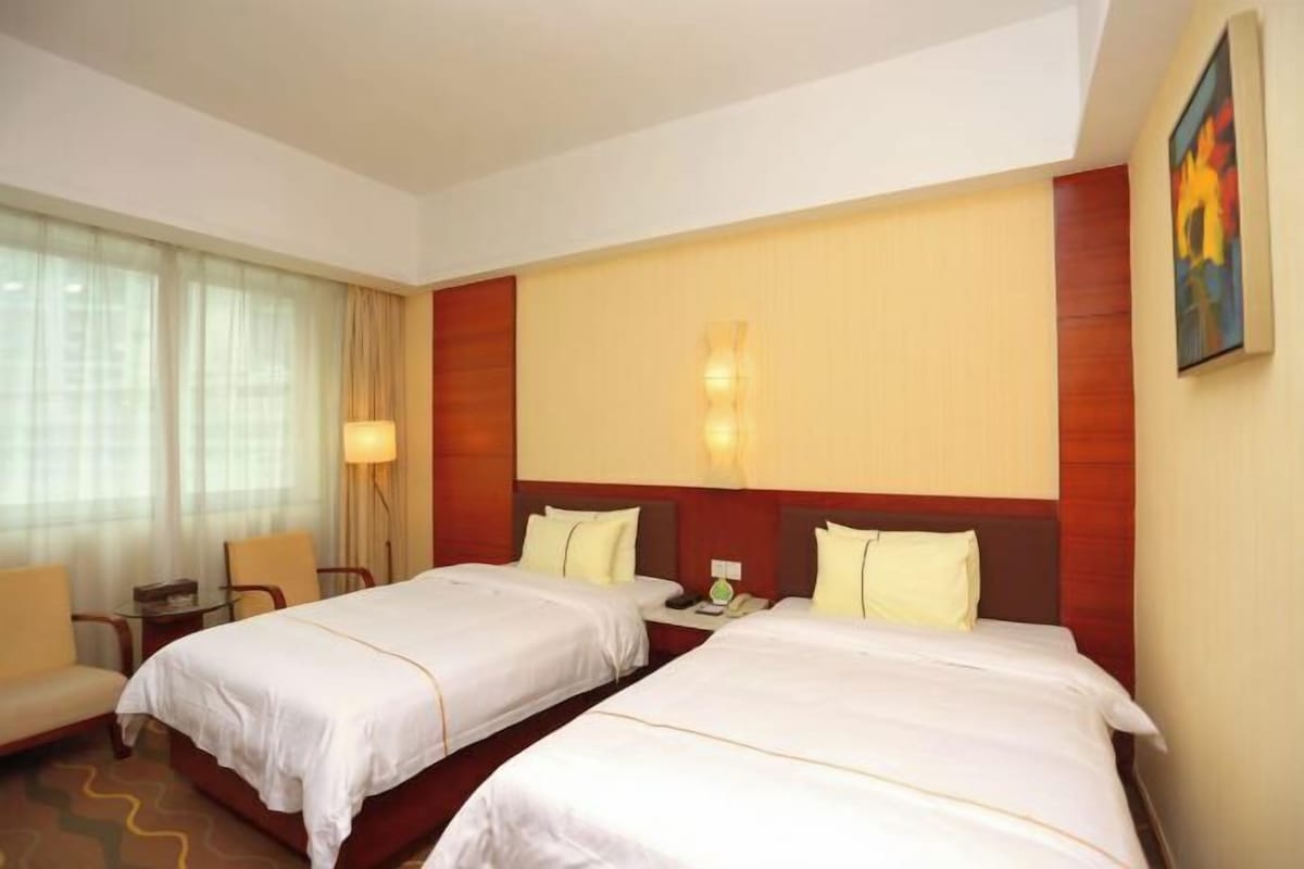 Habitación de hotel con dos camas, un escritorio, una silla, una lámpara y un cuadro en la pared.