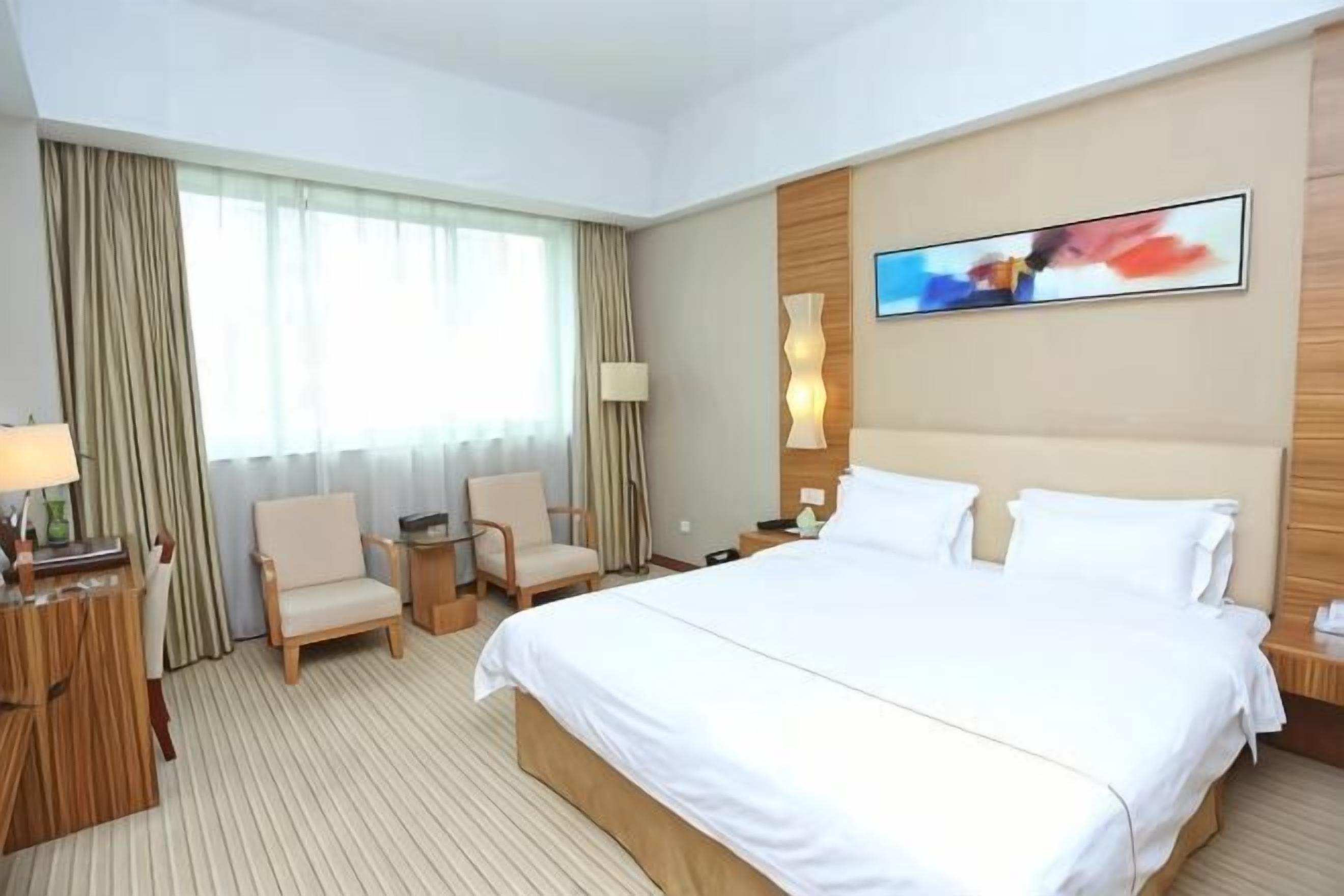 Une chambre d’hôtel avec un grand lit, deux chaises, un bureau avec une lampe et un tableau au mur.
