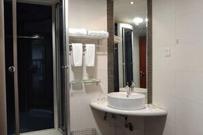 Une salle de bain avec une douche à parois de verre, un lavabo blanc avec un miroir et un porte-serviettes avec plusieurs serviettes.
